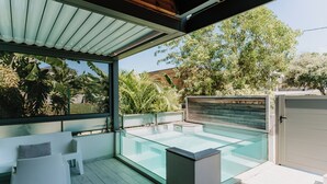 A modern outdoor pool area with glass walls, a wooden deck, and a seating area with white chairs. - Habitation I'SEO Adult Only (Sainte-Anne)