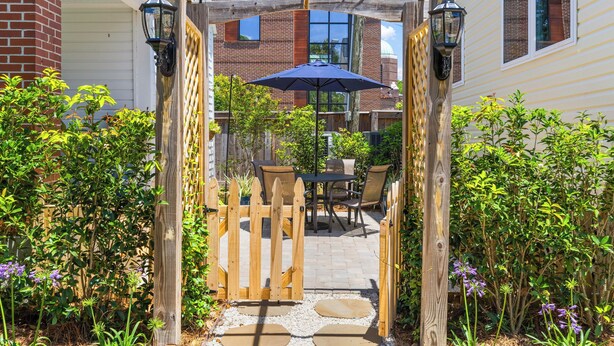 A wooden pergola with a table and chairs underneath, surrounded by greenery and a brick building in the background. - Charming Cottage in Downtown Charleston (Charleston)
