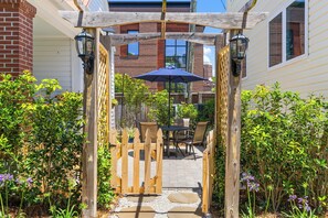 A wooden pergola with a table and chairs underneath, surrounded by greenery and a brick building in the background. - Charming Cottage in Downtown Charleston (Charleston)