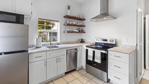 A modern kitchen with white cabinets, stainless steel appliances, and wooden shelves. - Charming Cottage in Downtown Charleston (Charleston)
