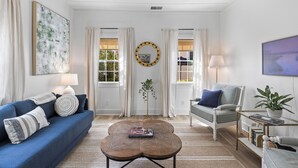 A living room with a blue sofa, a round coffee table, a grey armchair, and a floor lamp. - Charming Cottage in Downtown Charleston (Charleston)