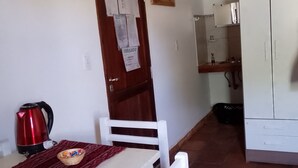 A small kitchen with a white cabinet, a red kettle, and a wooden door with papers. - Abril (Cafayate)