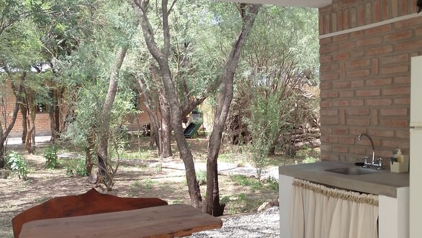 An outdoor patio with a wooden table and benches, a brick wall, and a sink. - Abril (Cafayate)