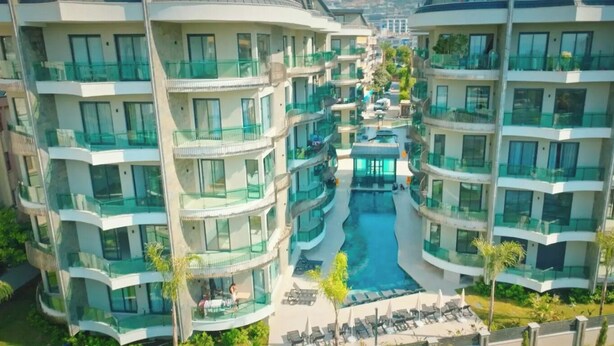 Een modern hotel met meerdere verdiepingen, balkons, een centraal gelegen zwembad en buitenzitplaatsen.