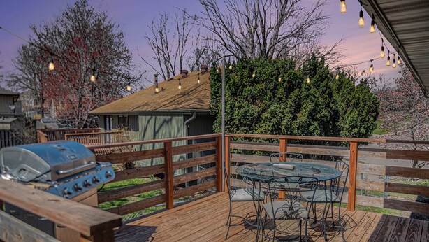 A wooden deck with a barbecue grill, a glass table with metal chairs, and string lights.