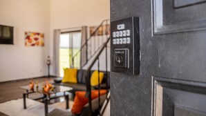 A modern interior with a staircase, a living area with a sofa and coffee table, and a door with a keypad lock.