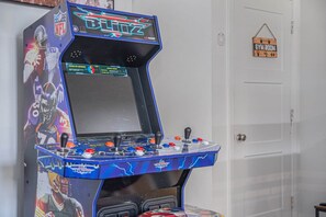 Máquina de videojuegos con la marca NFL, un panel de control con botones y palancas, y una puerta con un letrero que dice 'Sala de Gimnasia'.