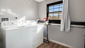 A laundry area with a washing machine, a window with curtains, and a hose.
