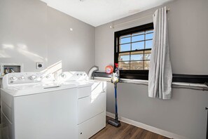 Un área de lavandería con lavadora, una ventana con cortinas y una manguera.