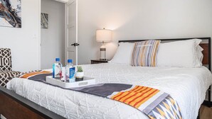 A neatly made bed with a white comforter, striped pillows, and a tray with toiletries.
