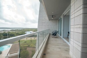 Un balcone con ringhiera in vetro che si affaccia su una piscina e un paesaggio collinare.