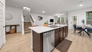 A modern kitchen with a central island, a dining area with a table and chairs, and a staircase leading to another level. - Luxurious 4 Bed Duplex Getaway! (Denton)
