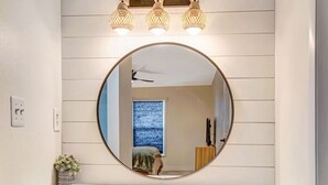 A bathroom vanity with a round mirror, a blue stool, and three wall-mounted lights. - Tropical Oasis with Pool, Spa, Putting Green & Game Room (Bradenton)
