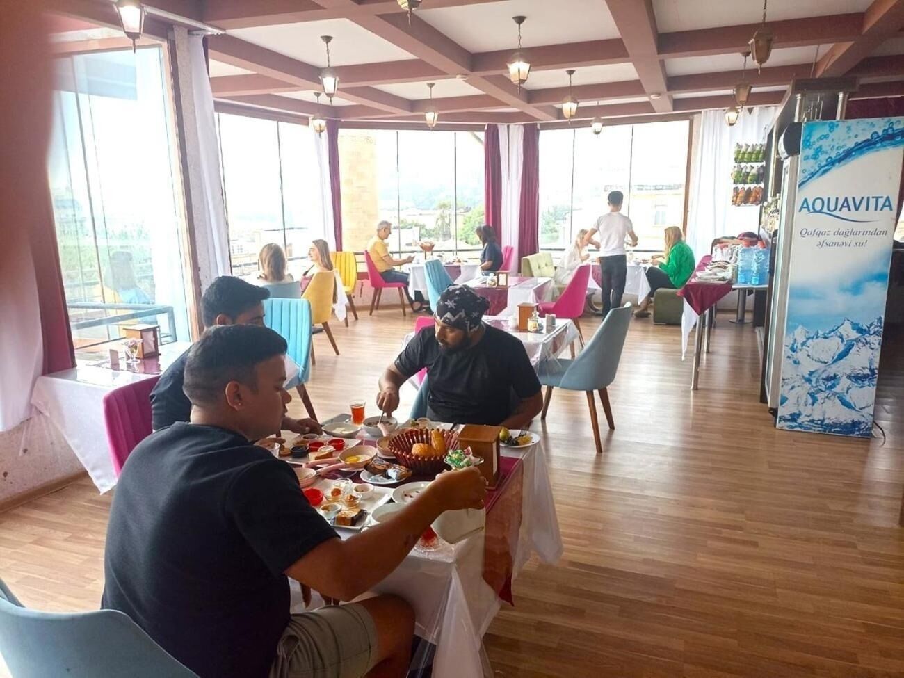 Un espace repas avec des tables et des chaises, de grandes fenêtres et une banderole publicitaire pour AQUAVITA.