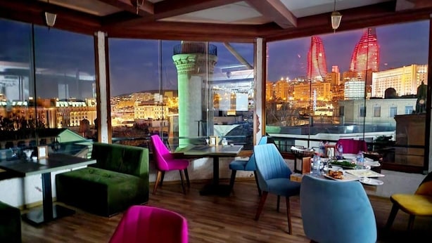 A restaurant with a city view, featuring a bar area, colorful chairs, and a dining table set for two. - Soffia Hotel Old City Baku (Baku)