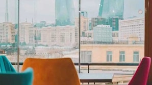 A room with large windows offering a view of a cityscape with modern buildings and a tower. - Soffia Hotel Old City Baku (Baku)