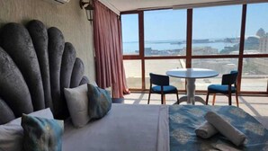 A hotel room with a bed, a round table with two chairs, and a large window offering a view of the sea and cityscape. - Soffia Hotel Old City Baku (Baku)