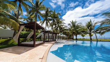 A poolside area with a pergola, lounge chairs, and palm trees.