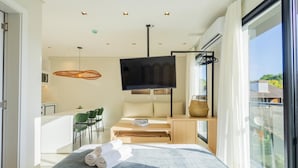 Una habitación moderna con televisión, zona de comedor y balcón con vistas.