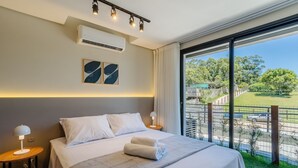 Habitación de hotel con una cama grande, una mesita de noche, un equipo de aire acondicionado y vistas a un área exterior cercada.