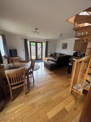 A spacious living area with a wooden floor, a dining table with chairs, a sofa, and a kitchen area with wooden cabinets. - Merlin’s lodge, countryside listing with a hot tub and disabled access (Long Bennington)
