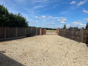 A gravel driveway leading to a gated area with a wooden fence and a brick wall. - Merlin’s lodge, countryside listing with a hot tub and disabled access (Long Bennington)