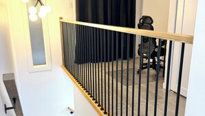 Een trap met een houten leuning en zwarte spijbels, leidend naar een kamer met een zwart gordijn en een stoel.