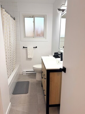 Ein Badezimmer mit Toilette, Waschbecken mit Spiegel und einer Duschtasse mit Ananasmuster.