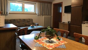 Un coin repas avec une table en bois, des chaises et un vase rempli de fleurs. Il y a une fenêtre avec des rideaux et un radiateur.