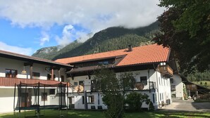 Un chalet traditionnel avec un toit recouvert de tuiles rouges, un balcon en bois et un petit jardin.