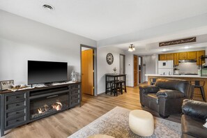 Ein modernes Wohnzimmer mit Kamin, Fernseher und einer Küche im Hintergrund.