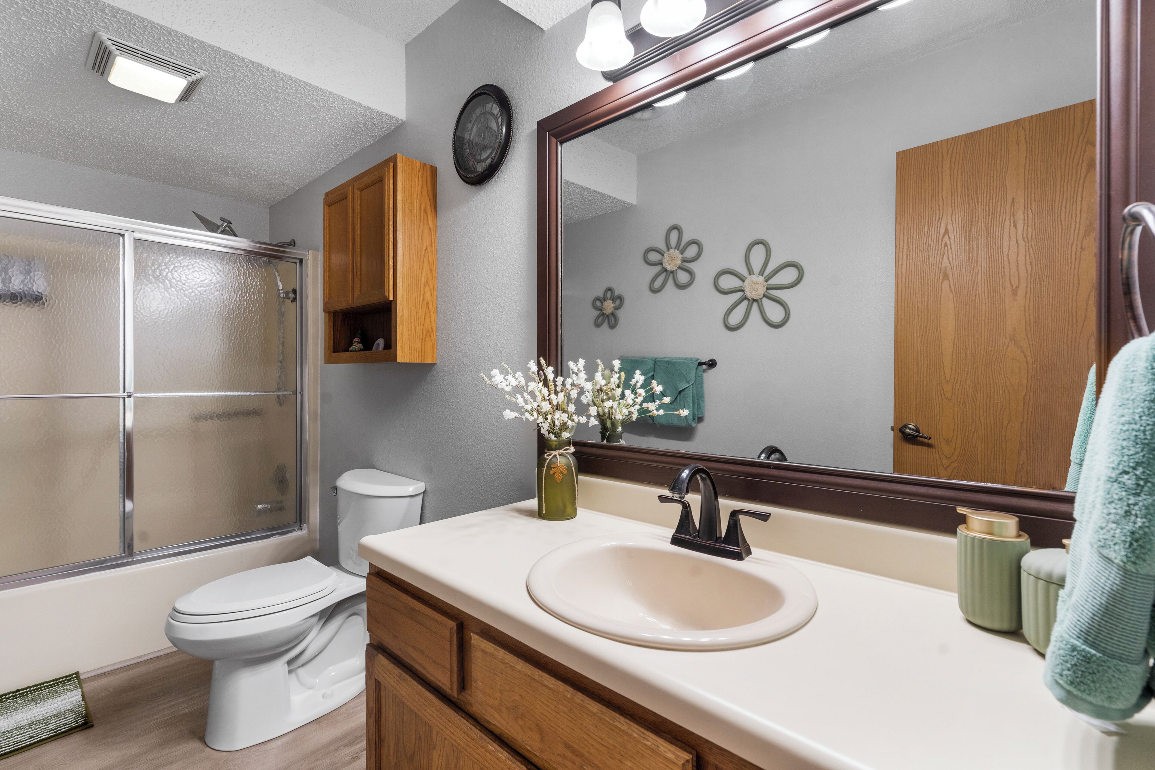 A bathroom with a glass shower enclosure, a toilet, a sink with a mirror above it, and wooden cabinets.