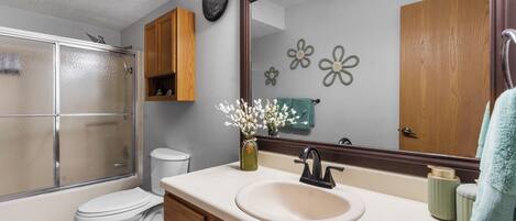 A bathroom with a glass shower enclosure, a toilet, a sink with a mirror above it, and wooden cabinets.