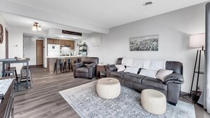 Una sala de estar moderna con un sofá gris, una mesa de comedor y una cocina al fondo.