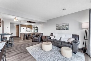 Ein modernes Wohnzimmer mit einem grauen Sofa, einem Esstisch und einer Küche im Hintergrund.