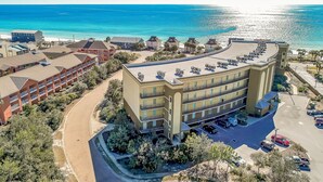 Ein mehrstöckiges Hotel mit bogenförmiger Fassade, Parkplatz und Blick auf den Strand.