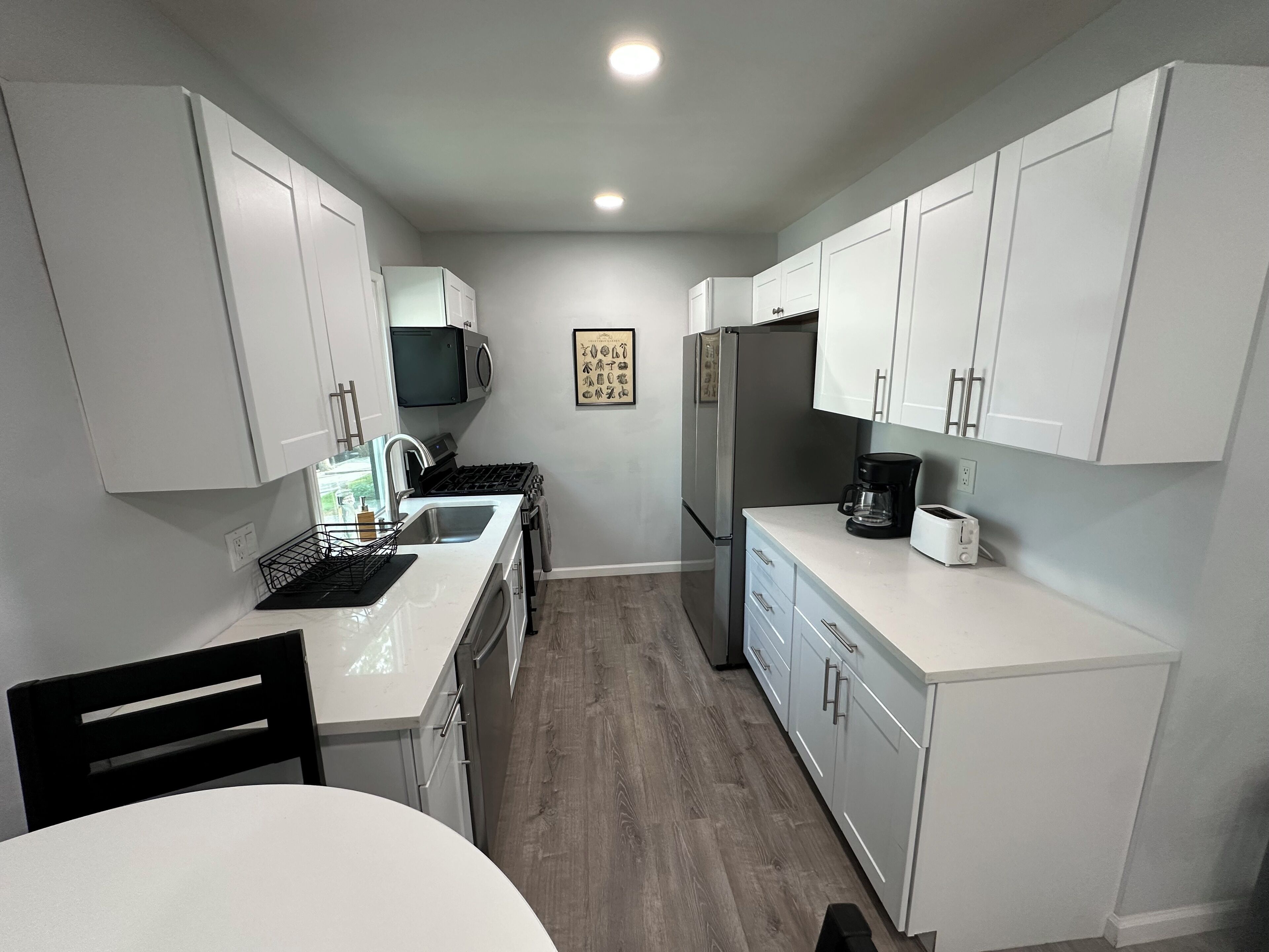 A compact kitchen with white cabinets, a microwave, a refrigerator, a coffee maker, and a sink.