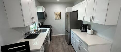 A compact kitchen with white cabinets, a microwave, a refrigerator, a coffee maker, and a sink.