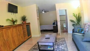 A living room with a sofa, a coffee table, a TV mounted on the wall, and a bed in the background. - Torraille Waterfall Villas - Unit 1 (Soufrière)