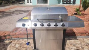 A portable stainless steel grill with five burners and a water pan, placed on a stone patio. - Torraille Waterfall Villas - Unit 1 (Soufrière)