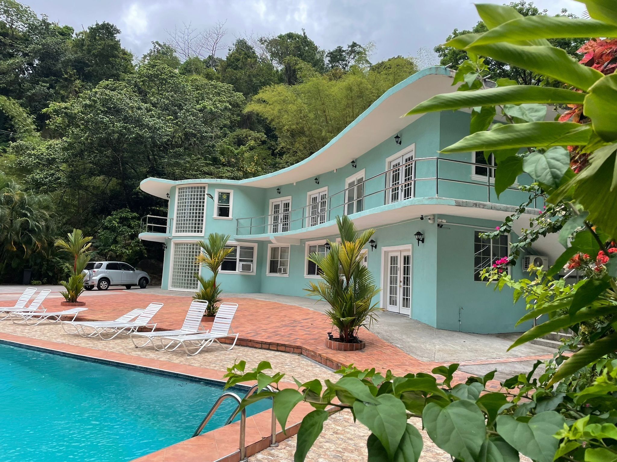 A two-story building with a swimming pool, white lounge chairs, and potted plants.