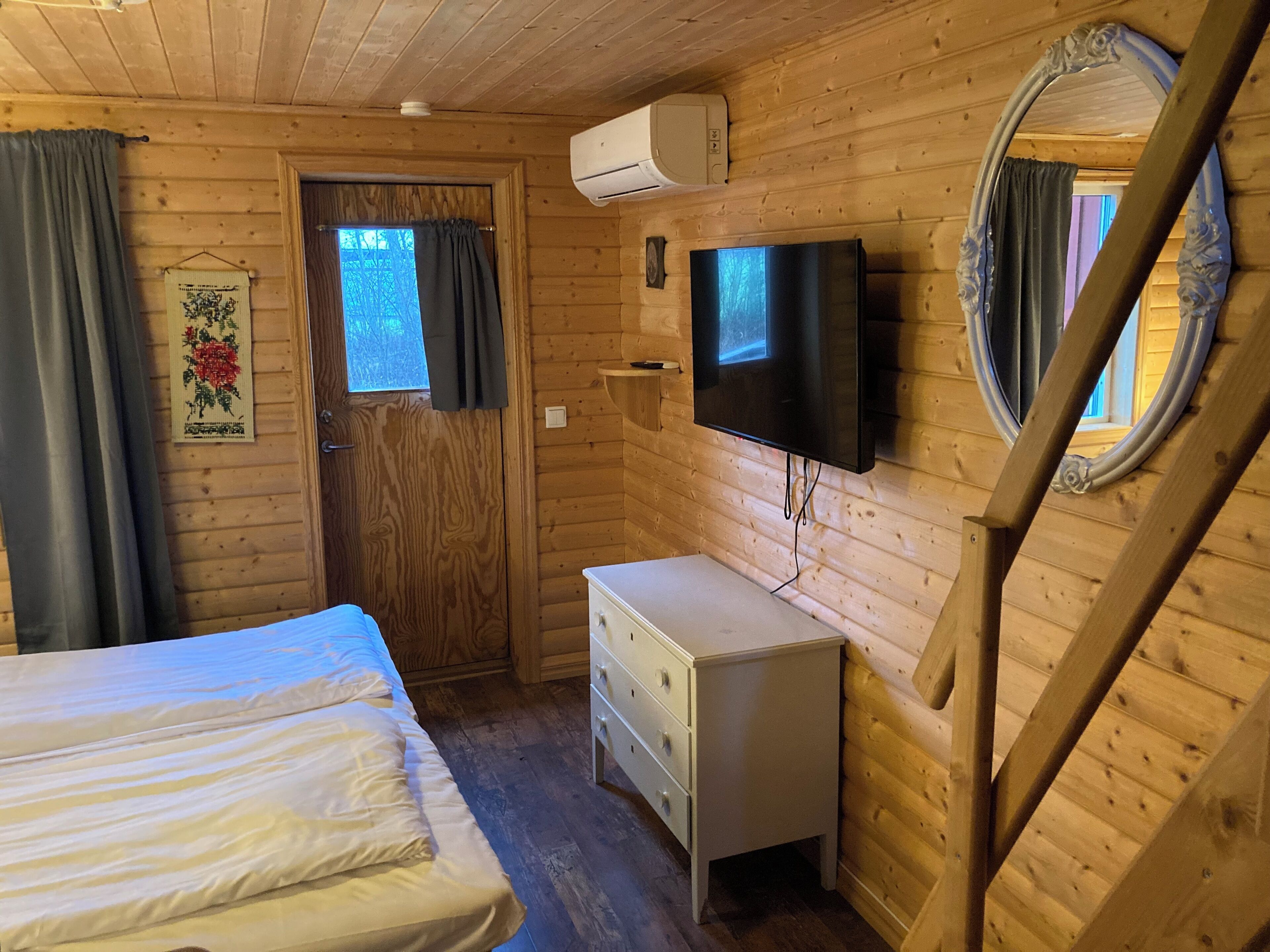Una camera in una baita di legno con un letto, una cassettiera, una TV a parete e una finestra con tende.
