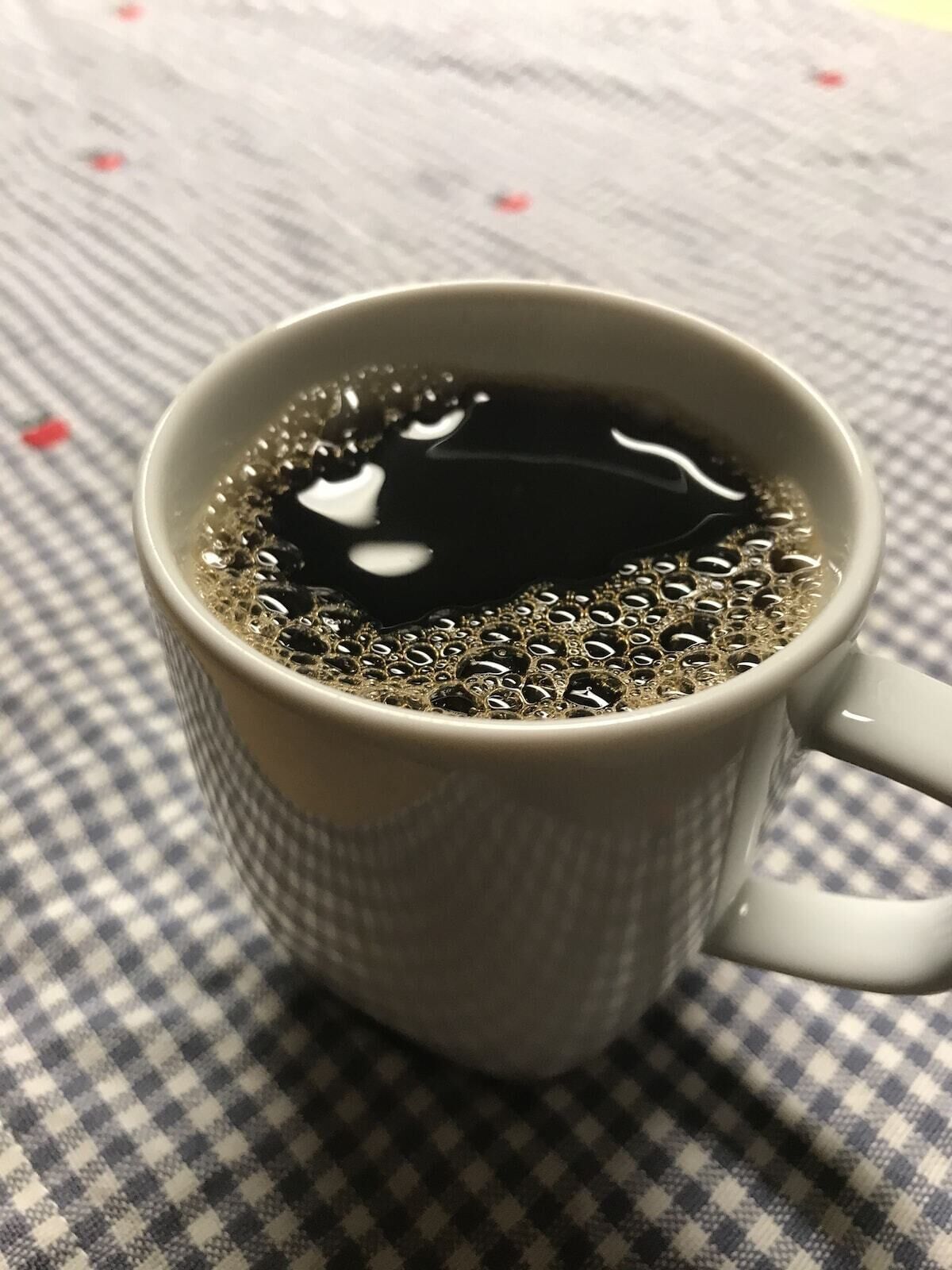 A cup of black coffee on a checkered tablecloth.