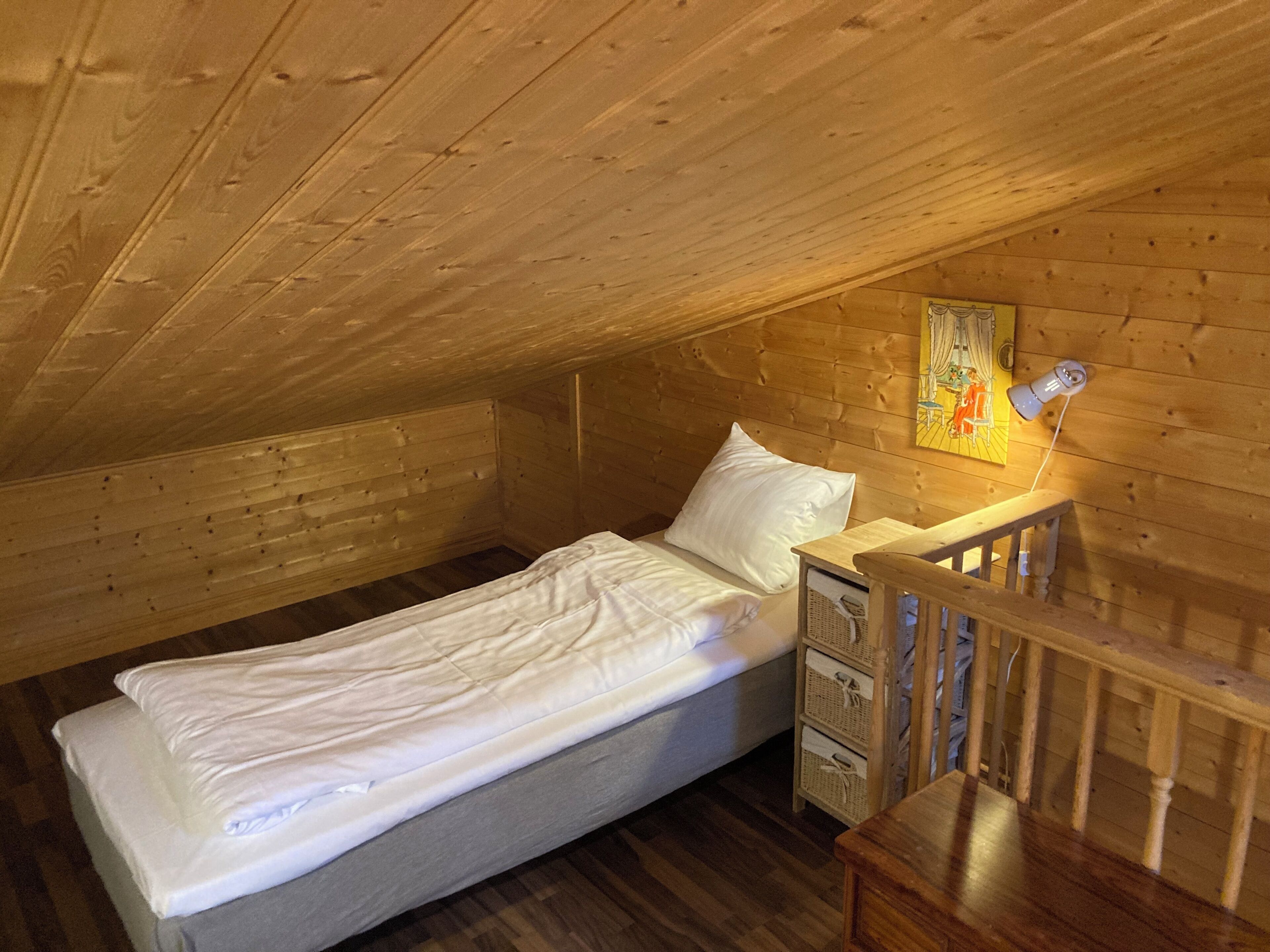 Habitació petita i acollidora amb un llit individual, parets de fusta i un sostre inclinat.
