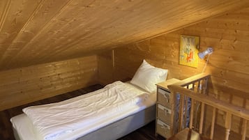 Habitació petita i acollidora amb un llit individual, parets de fusta i un sostre inclinat.