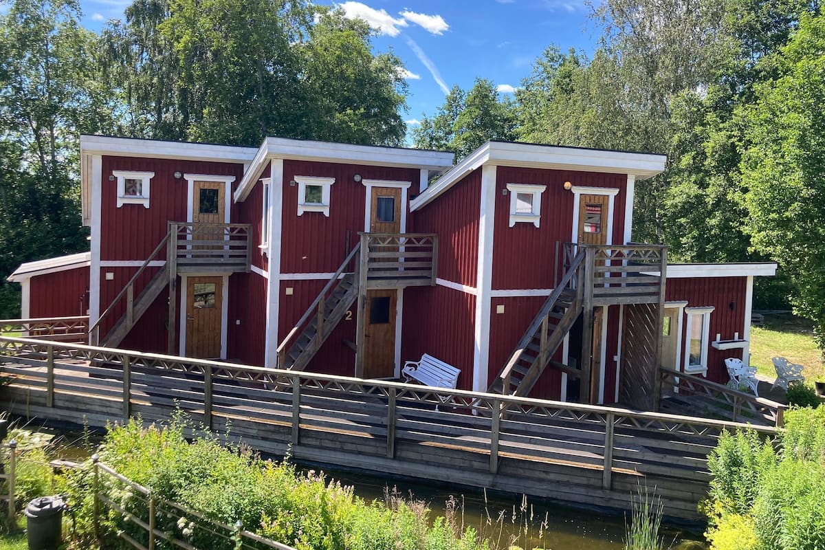 Una cabaña roja de madera con varios niveles, escaleras de madera y una pequeña terraza.