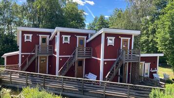 A red wooden cabin with multiple levels, wooden stairs, and a small deck area.