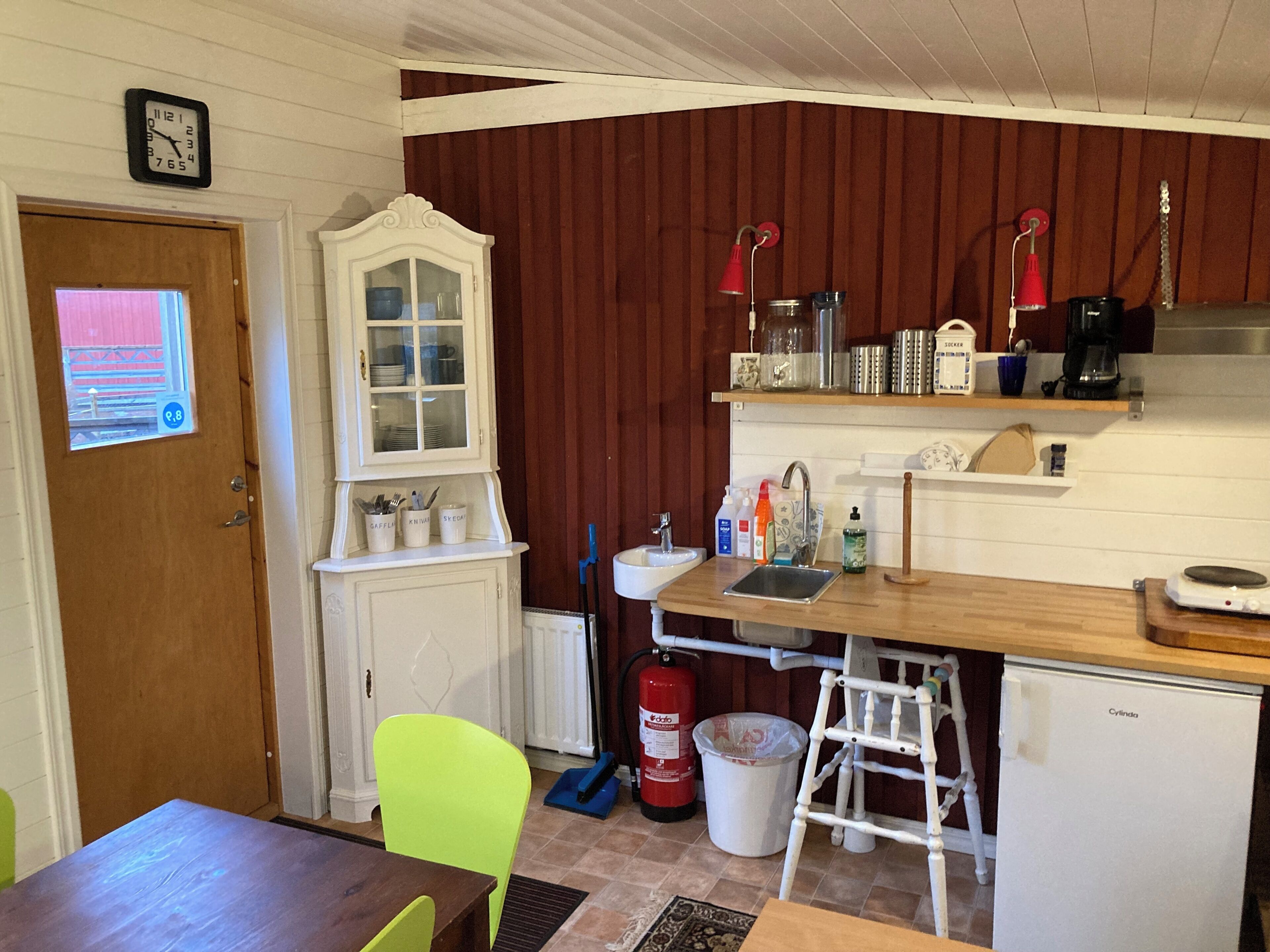 A compact kitchen with a wooden table, a green chair, a white cabinet, and a small refrigerator.