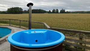 Een hottub op een houten terras, met uitzicht op een veld en bomen.