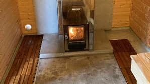 Een houtkachel met een metalen schoorsteen, een stapel steen bovenop en een betonnen vloer.